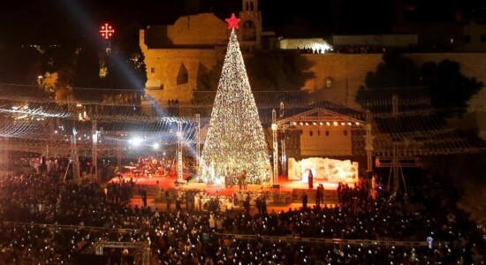 Palestinos acendem árvore de Natal na Praça da Manjedoura, em frente à Igreja da Navidade, em Belém, na Cisjordania ocupada