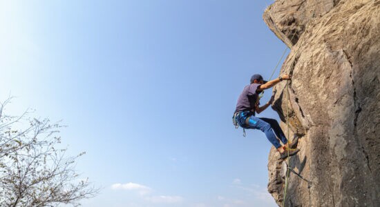 young-male-climber-on-a-rocky-cliff-against-a-blue-sky
