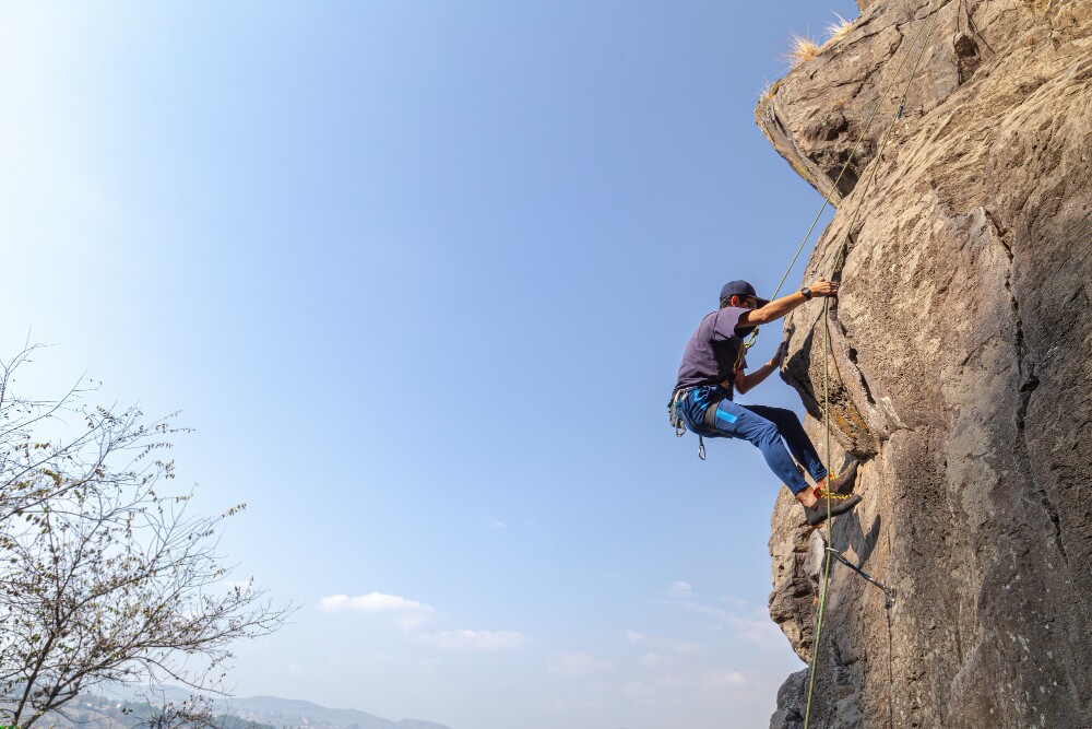 young-male-climber-on-a-rocky-cliff-against-a-blue-sky
